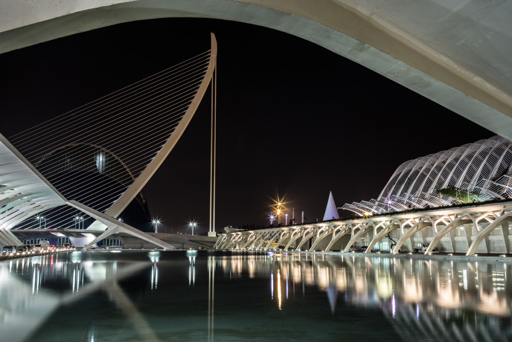 Modernes Bauwerk bei Nacht mit geschwungenen Strukturen und beleuchteten Wasserflächen.