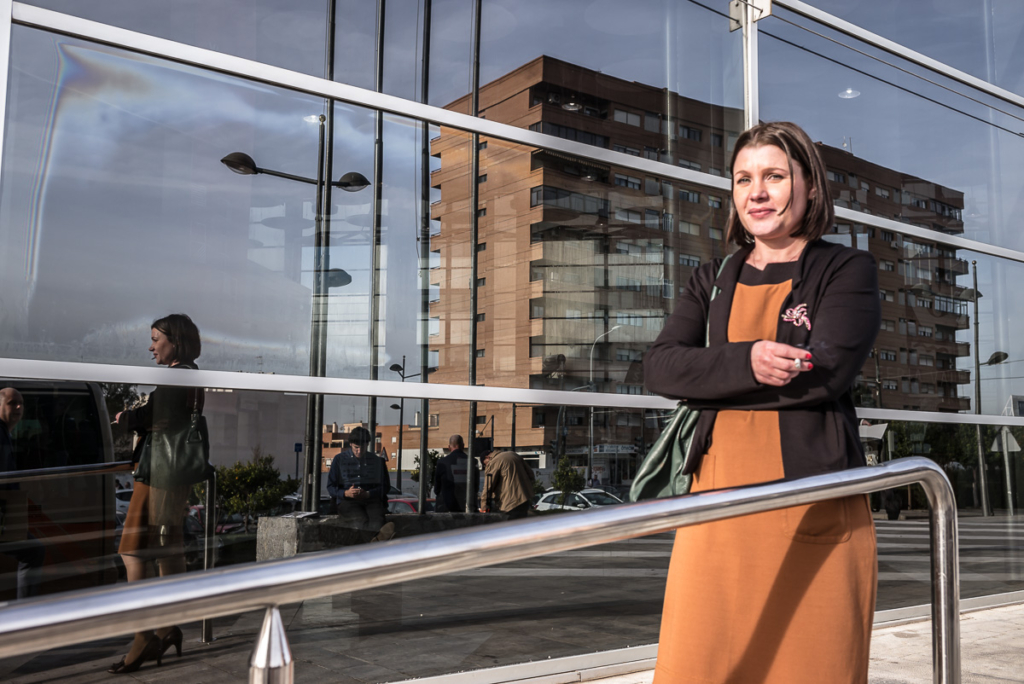 Frau vor modernem Gebäude mit Spiegelung von Personen und Stadt im Glas, braunes Kleid, Blazer.
