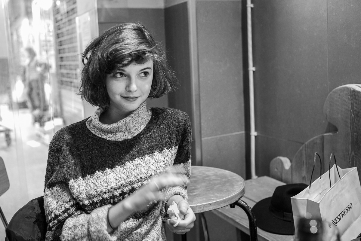 Frau in Café, runder Tisch, Nespresso-Tasche, Hut, Schwarz-Weiß-Foto.